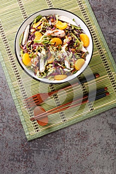 Chinese-Inspired Chicken Salad with tangerines, red cabbage, Chinese cabbage, carrots and noodles close up in the bowl. Vertical