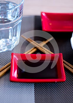 Chinese / Japanese red recipients full of soy sauce with sticks and a glass of water