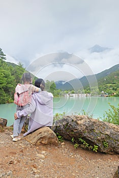 Chinese kid leaning against moms shoulder by beautiful lake