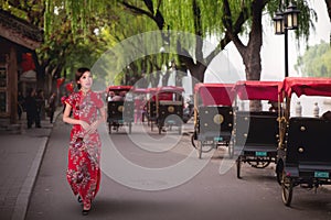 Chinese lady in red cheongsam dress walking near a Tourists riding Beijing traditional rickshaw