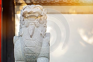 Chinese lion figurine, stone sculpture in front of Chinese shrine wall with sun flare background