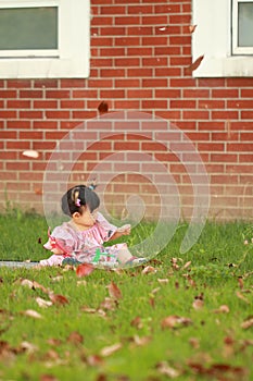 A Chinese little baby girl play leaves on the lawn