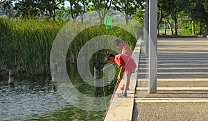 Chinese little boys playing fishing near a pond on a summer day, using a fishing net ant a stick like fishing rod