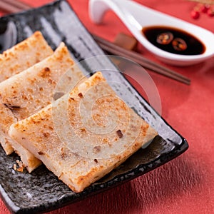 Chinese lunar new year food concept, Delicious turnip radish cake, local cuisine in restaurant with soy sauce on red background,