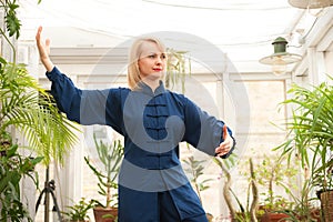 Chinese martial arts tai chi. Woman practicing Taijiquan discipline in a greenhouse with flowers