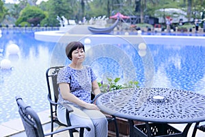 Chinese middle-aged woman sitting on a chair beside the pool