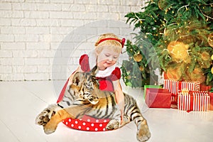 Chinese new year 2022. girl hugs symbol of year tiger baby near Christmas tree in white hall against background of brick