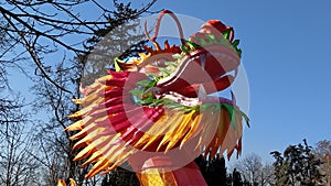 Chinese New Year. Bright red-orange dragon in the park. Traditional Chinese holiday decoration. The dragon`s mouth is open. Long