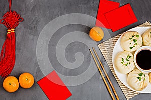 Chinese New Year decoration with dumplings, tangerines, soy sauce, chopsticks, red envelopes on gray concrete background. Happy