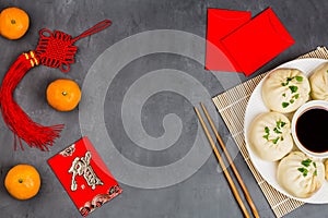 Chinese New Year decoration with dumplings, tangerines, soy sauce, chopsticks, red envelopes on gray concrete background. Happy