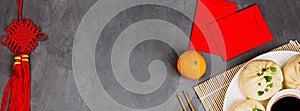 Chinese New Year decoration with dumplings, tangerines, soy sauce, chopsticks, red envelopes on gray concrete background. Happy