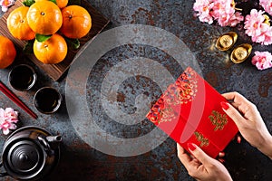 Chinese new year festival decorations. Woman hand holding pow or red packet, orange and gold ingots on a black stone background.