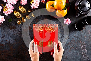 Chinese new year festival decorations. Woman hand holding pow or red packet, orange and gold ingots on a black stone texture