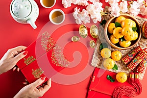 Chinese new year festival decorations. Woman hand holding pow or red packet, orange and gold ingots on a red background. Chinese