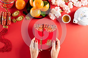 Chinese new year festival decorations. Woman hand holding pow or red packet, orange and gold ingots on a red background. Chinese