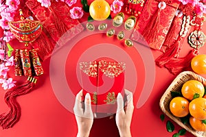 Chinese new year festival decorations. Woman hand holding pow or red packet, orange and gold ingots on a red background. Chinese