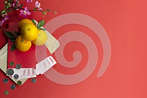 Chinese new year fresh oranges and angpao pocket with wooden board and cherry blossom flower on red paper background