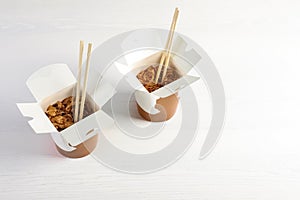 Chinese noodles in paper box on white wooden table, space for text.