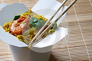 Chinese noodles with shrimps and vegetables in box on bamboo mat. Chinese food concept