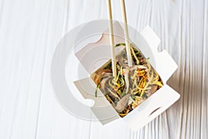 Chinese noodles in takeaway box on wooden background. Food.