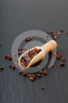 Chinese peppercorn, Sichuan pepper in wooden scoop on black slate stone plate with copy space
