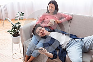 Chinese Spouses Relaxing Watching TV Sitting On Sofa At Home