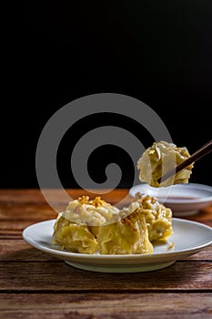 Chinese Steamed Dumpling, Shumai on white dish served with soy sauce on wooden table on black background. Delicious Dimsum pork