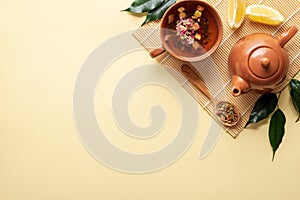 Chinese tea ceremony. Ceramic teapot, teacup, green leaves, wooden spoon with dried tea on bamboo mat on yellow background. Top