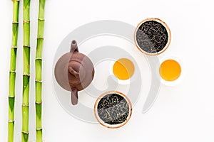 Chinese tea ceremony concept. Tea pot, tea cup, dry tea leaves, bamboo mat on white background top view copy space