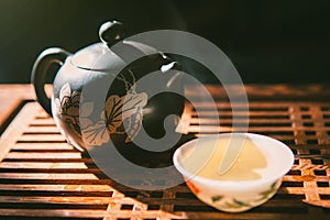 Chinese tea ceremony. Teapot and a cup of green puer tea on wooden tabl with small amount of vapour. Asian traditional culture.