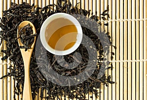 Chinese tea in white ceramic cup and dried tea leaves in wooden spoon