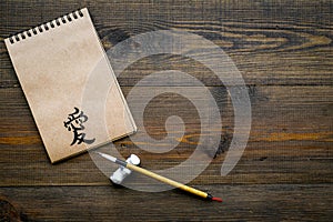 Chinese traditional calligraphy concept. Asian hieroglyph love in craft paper notebook near special writting pen on dark