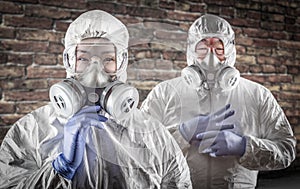 Chinese Woman and Man In Gas Masks, Goggles and Hazmat Suites Against Brick Background photo