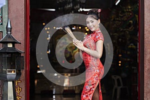 Chinese woman in a red cheongsam dress holding incense pay homage to Chinese god at shrine. Concept to celebrate Chinese New Year photo