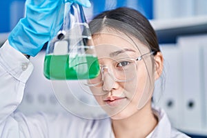Chinese woman scientist holding test tube over eye at laboratory