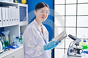 Chinese woman scientist smiling confident reading book at laboratory