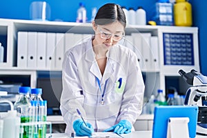 Chinese woman scientist writing on document using touchpad at laboratory