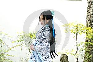 Chinese woman in traditional Blue and white Hanfu dress sit next to bonsai