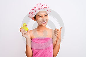 Chinese woman wearing shower towel and cap holding duck toy over isolated white background happy with big smile doing ok sign,