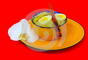 Chinese wonton noodles with soup in a stoneware bowl with single orchid flower on the side