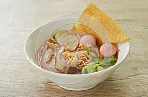 Chinese yellow egg noodles with fish ball and chop pork in red soup on bowl