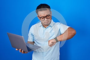 Chinese young man using computer laptop checking the time on wrist watch, relaxed and confident