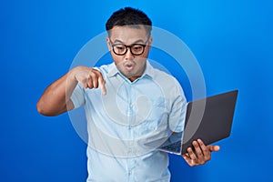 Chinese young man using computer laptop pointing down with fingers showing advertisement, surprised face and open mouth