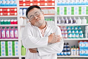 Chinese young man working at pharmacy drugstore hugging oneself happy and positive, smiling confident