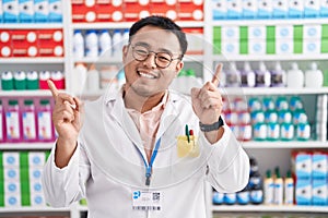 Chinese young man working at pharmacy drugstore smiling confident pointing with fingers to different directions