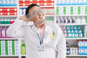 Chinese young man working at pharmacy drugstore smiling confident touching hair with hand up gesture, posing attractive and