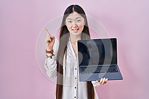 Chinese young woman holding laptop showing screen smiling happy pointing with hand and finger to the side