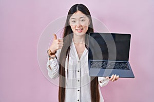 Chinese young woman holding laptop showing screen smiling happy and positive, thumb up doing excellent and approval sign