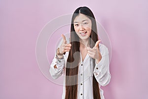 Chinese young woman standing over pink background pointing fingers to camera with happy and funny face