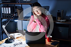 Chinese young woman working at the office at night sleeping tired dreaming and posing with hands together while smiling with